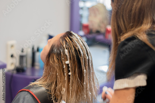 Hairdresser putting hair mousse in the hair of a blonde woman.