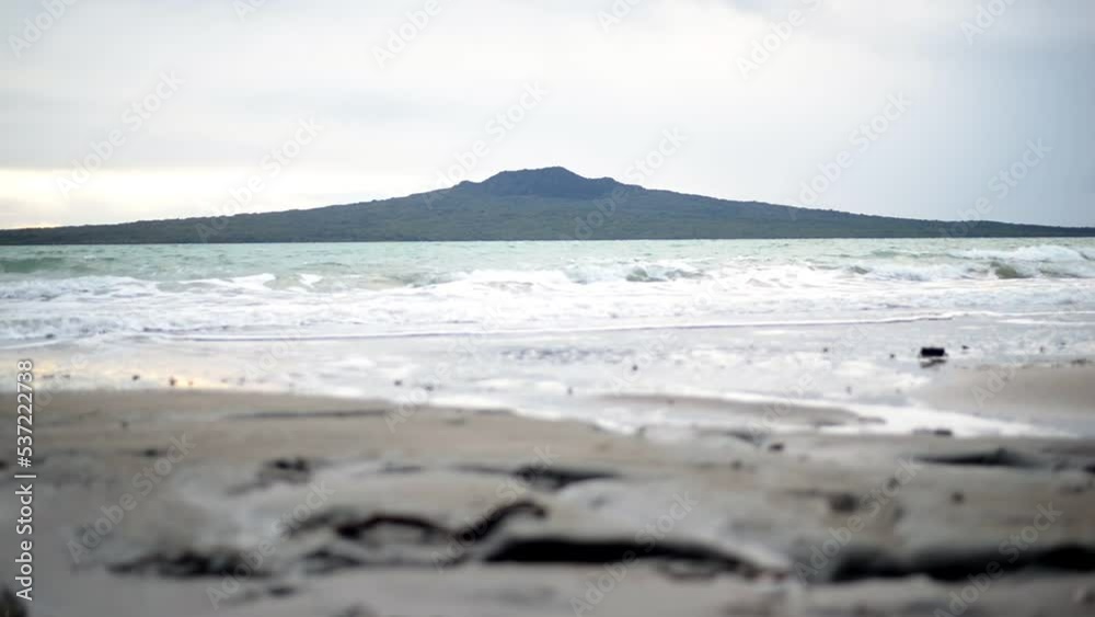 Low shot of waves rolling into a beach with Rangitoto Island in the background Low shot of waves rolling into a beach with Rangitoto Island in the background
