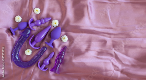 Purple silicone sex toys on pink silk background. An erotic toy for entertainment. Various anal plugs. Banner with space for text