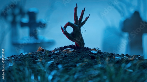Zombie hand makes okay gesture out of grave. Holiday event halloween concept photo