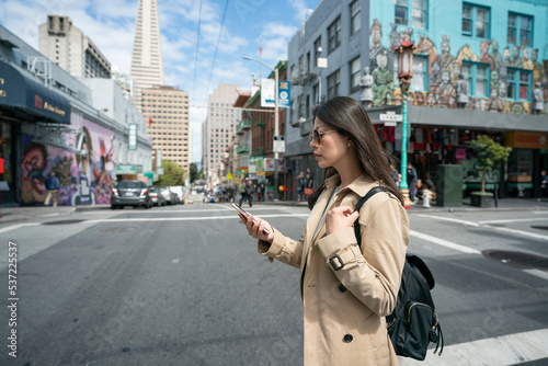 asian Japanese businesswoman taking a look at her cellphone to check message while walking across street intersection in san Franciscoâs China town on her way to work