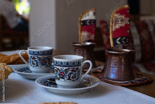 handpainted cups and cezve of natural turkish coffee served with cheburek dish on wooden table, drink cooked in sand with adding sugar, typical Crimean tatar restaurant in Odesa, Ukraine, detail
