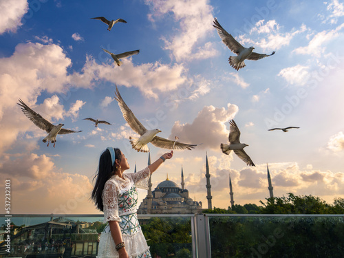 Lifestyle, Asian woman tourist feeding seagulls at view point in vacation. There is a Blue Mosque in the background in a blur. Popular tourist destination. Sultanahmet, Istanbul, Turkiye, Turkey