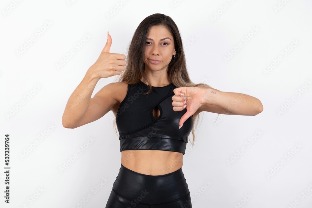 young beautiful woman wearing sportswear over white background showing thumbs up and thumbs down, difficult choose concept