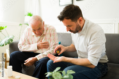 Caucasian man giving his medicine pills to his sick old father