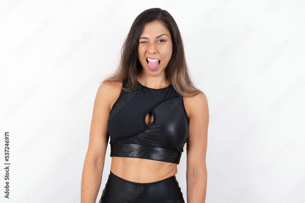 young beautiful woman wearing sportswear over white background sticking tongue out happy with funny expression. Emotion concept. young beautiful woman wearing sportswear over white background sticking tongue out happy with funny expression. Emotion concept.