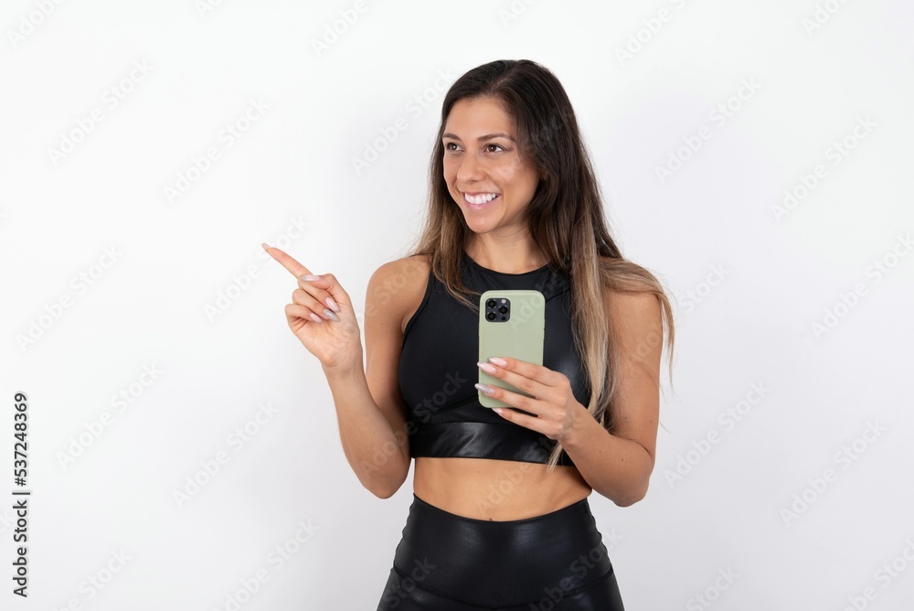 Wow!! excited young beautiful woman wearing sportswear over white background showing mobile phone with open hand gesture Wow!! excited young beautiful woman wearing sportswear over white background showing mobile phone with open hand gesture