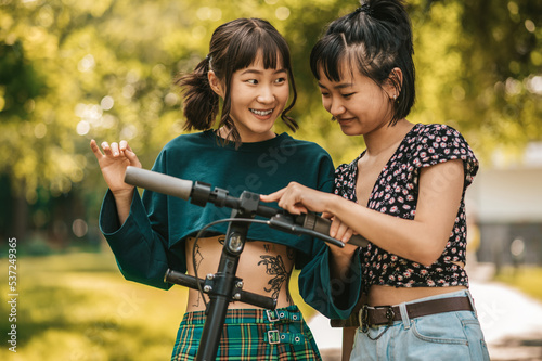 Two smiling girls with a scooter in the park