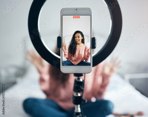 Live streaming, phone and black woman talking on video podcast in the bedroom of her house. Happy and excited girl or influencer speaking on the internet or social media with a mobile and ring light photo