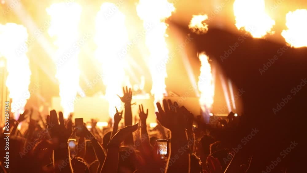 Silhouette hands of audience crowd people at night rock concert with colorful stage lights