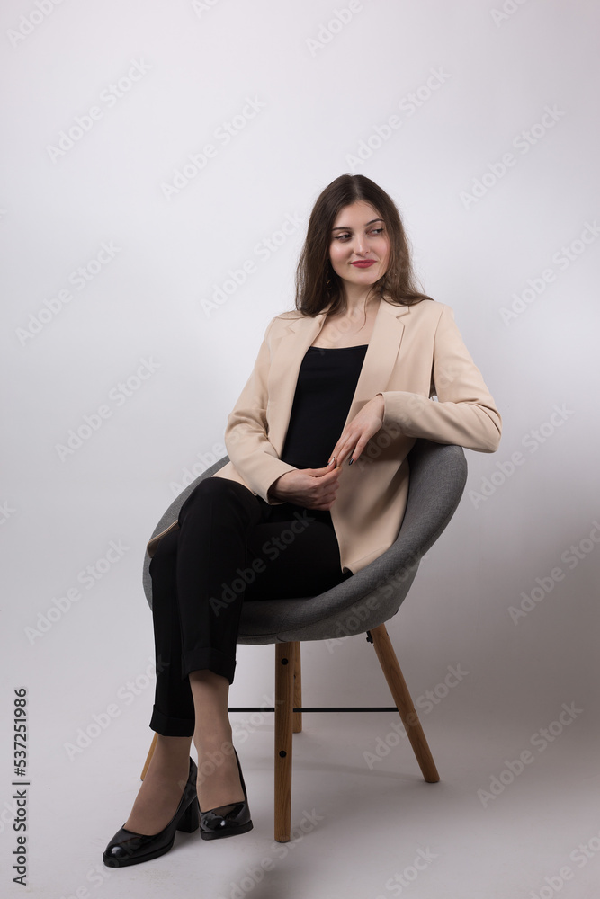 Portrait of a young brunette with long hair in the studio. Cute girl sitting on a chair on a white background.