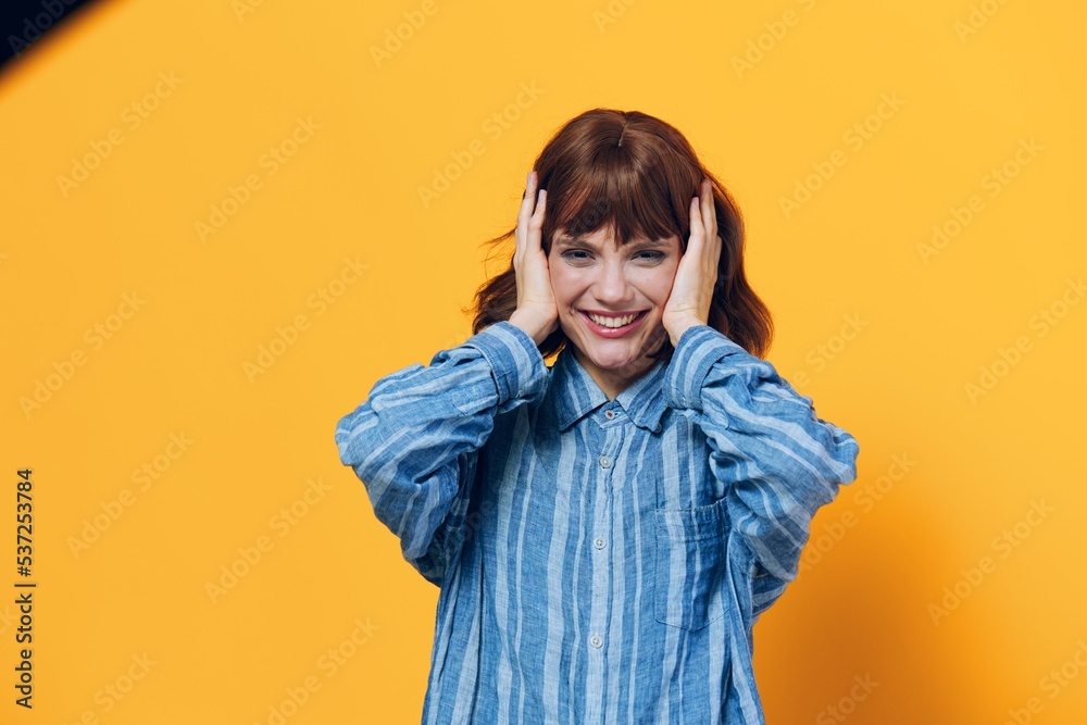 a happy, emotional woman smiles broadly with her hands on her head standing on a yellow background in a blue shirt a happy, emotional woman smiles broadly with her hands on her head standing on a yellow background in a blue shirt