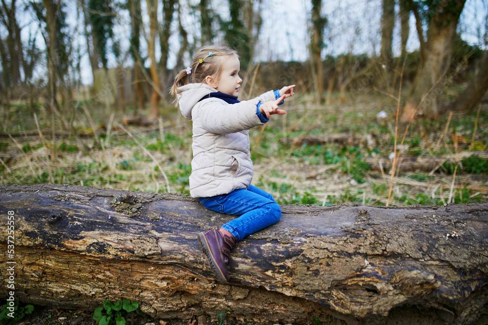 Adorable preschooler girl sitting on log and having fun in spring ...