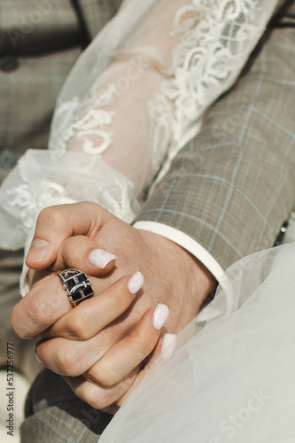 Outdoors close-up of the intertwined hands of the bride and groom, man and woman, hands in a white tulle dress and gray jacket, copy space.