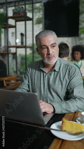 Older entrepreneur seated at coffee shop with laptop staring at screen. Closeup male senior executive working remotely using computer at cafe place in Vertical Video SS