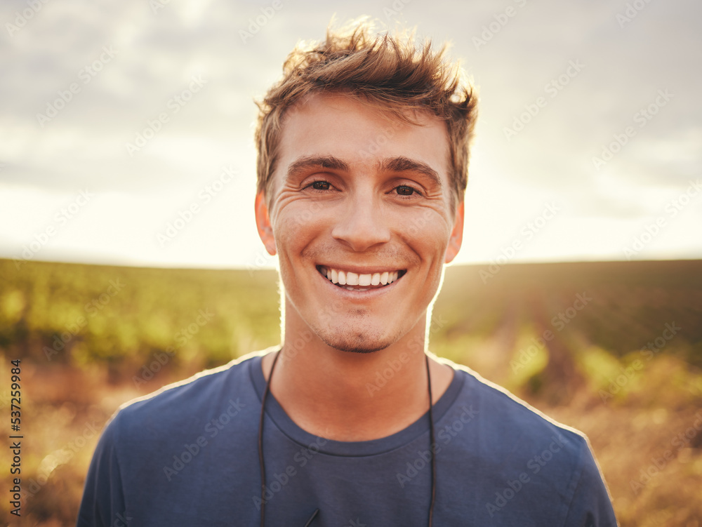Happy, face and nature with a man at sunset, enjoying freedom with a smile and standing on a field of grass in the day. Travel, vacation and morning with the portrait of a handsome young male outside Happy, face and nature with a man at sunset, enjoying freedom with a smile and standing on a field of grass in the day. Travel, vacation and morning with the portrait of a handsome young male outside