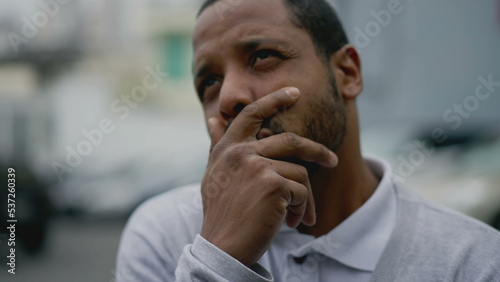 Anxious young man feeling despair and negative thoughts. African American person suffering from mental illness standing in street covering face with hand