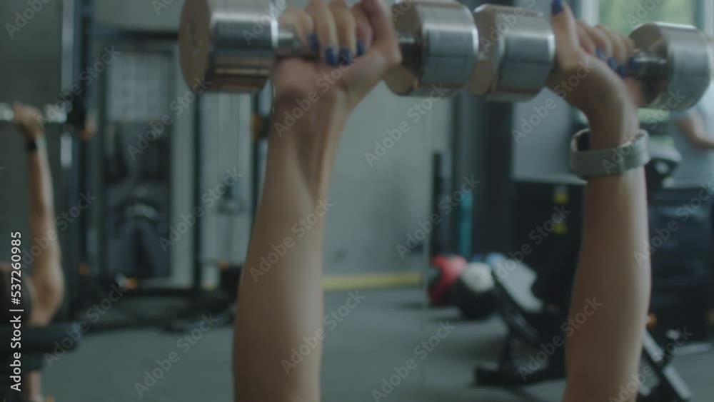 Close up handheld camera shot sporty woman doing dumbbell chest press exercise on bench while working out in gym