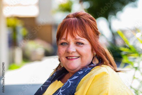 Headshot of happy smiling middle age woman wearing yellow in urban setting