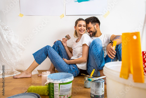 Young couple sitting on the floor choosing color for painting the wall in their home. photo