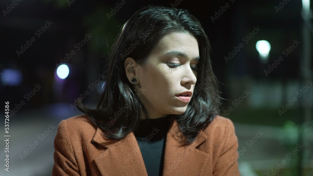 One lonely young woman walking at night in drizzle rain in downtown street. Sad depressed person with arms crossed walks in evening stroll with worried expression One lonely young woman walking at night in drizzle rain in downtown street. Sad depressed person with arms crossed walks in evening stroll with worried expression