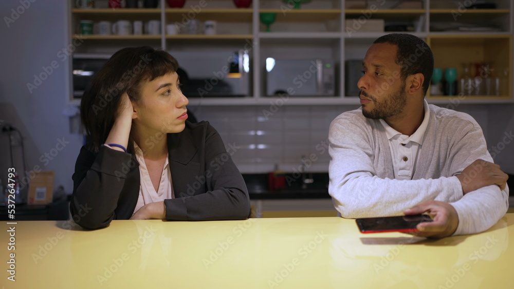 Two work colleagues in conversation at office kitchen table casually. Diverse people talking together Two work colleagues in conversation at office kitchen table casually. Diverse people talking together