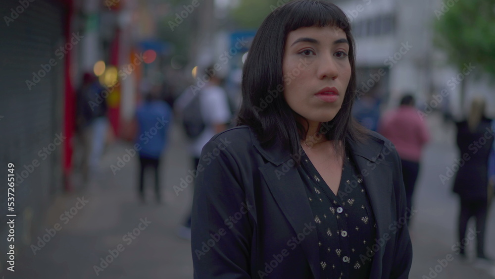 Stressed young hispanic woman standing in urban street fidgeting with hands. Preoccupied South American adult girl feeling nervous and preoccupation