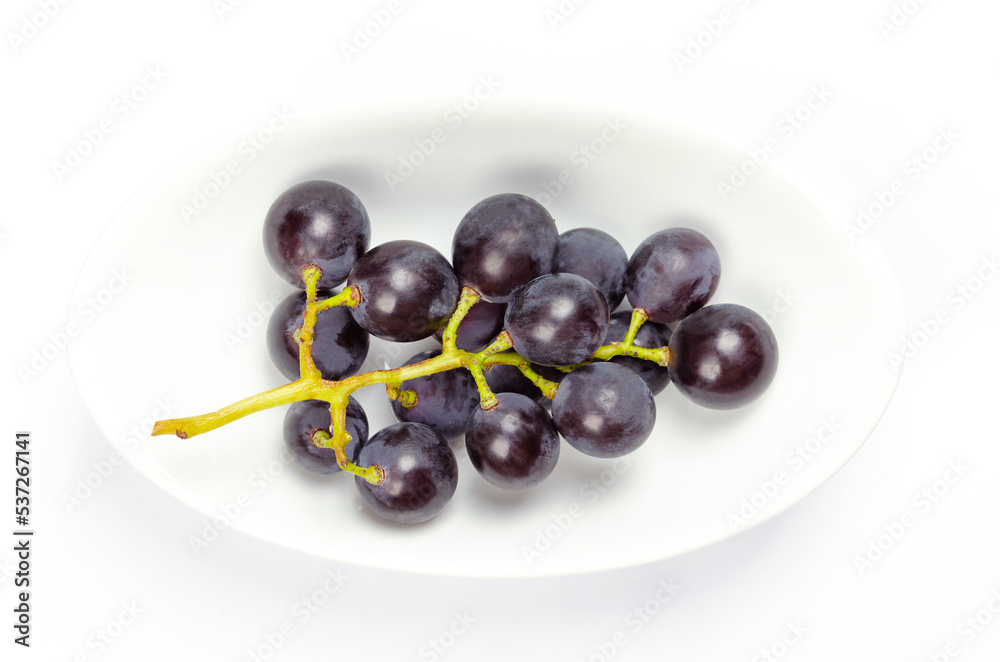 Common grape vines, in a white bowl. Freshly picked vines of ripe wild grapes, Vitis vinifera, with small dark purple grapes, showing a natural epicuticular pale wax bloom. Close up macro food photo. Common grape vines, in a white bowl. Freshly picked vines of ripe wild grapes, Vitis vinifera, with small dark purple grapes, showing a natural epicuticular pale wax bloom. Close up macro food photo.