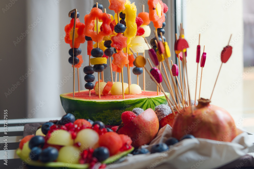 Fruit salad for a child's birthday. Various fruits are put on toothpicks and hammered into half of a watermelon. Watermelon, melon, blueberries, and pineapple. Hollow fruit and formed into balls