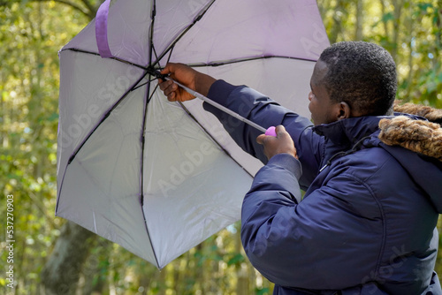 African man close an umbrella in a park in wintertime. Winter fashion. © Sheila