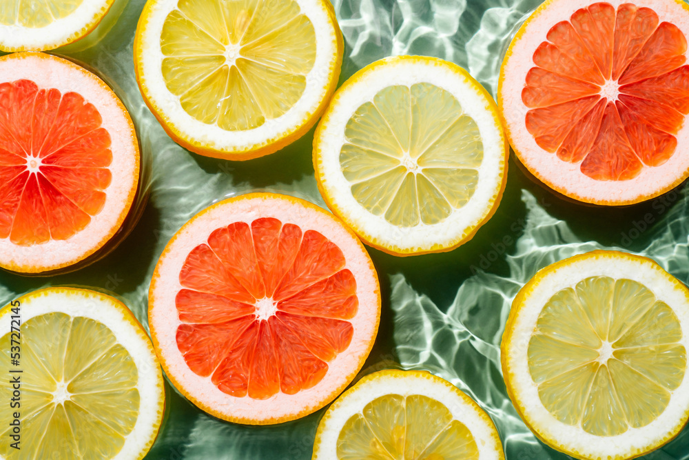 © Евгения Рубцова - Colorful background image of fruit citrus lemon, orange, grapefruit, slices in water splashing fresh transparent surface with flecks. Flat lay, top view. Summer beach tropical