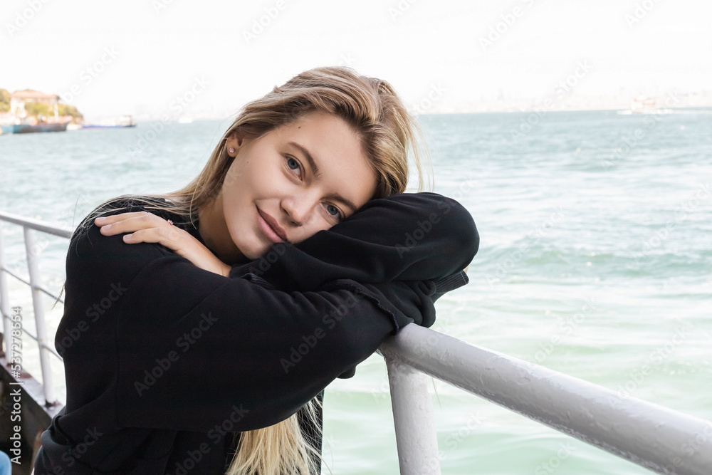 blonde young woman in black sweater looking at camera from ferry boat crossing bosphorus strait. blonde young woman in black sweater looking at camera from ferry boat crossing bosphorus strait.