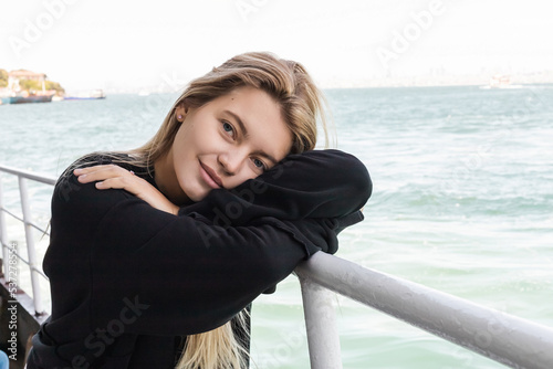 blonde young woman in black sweater looking at camera from ferry boat crossing bosphorus strait. © LIGHTFIELD STUDIOS
