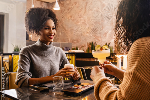 Happy girlfriends women couple drinking cocktails at fusion bar restaurant photo