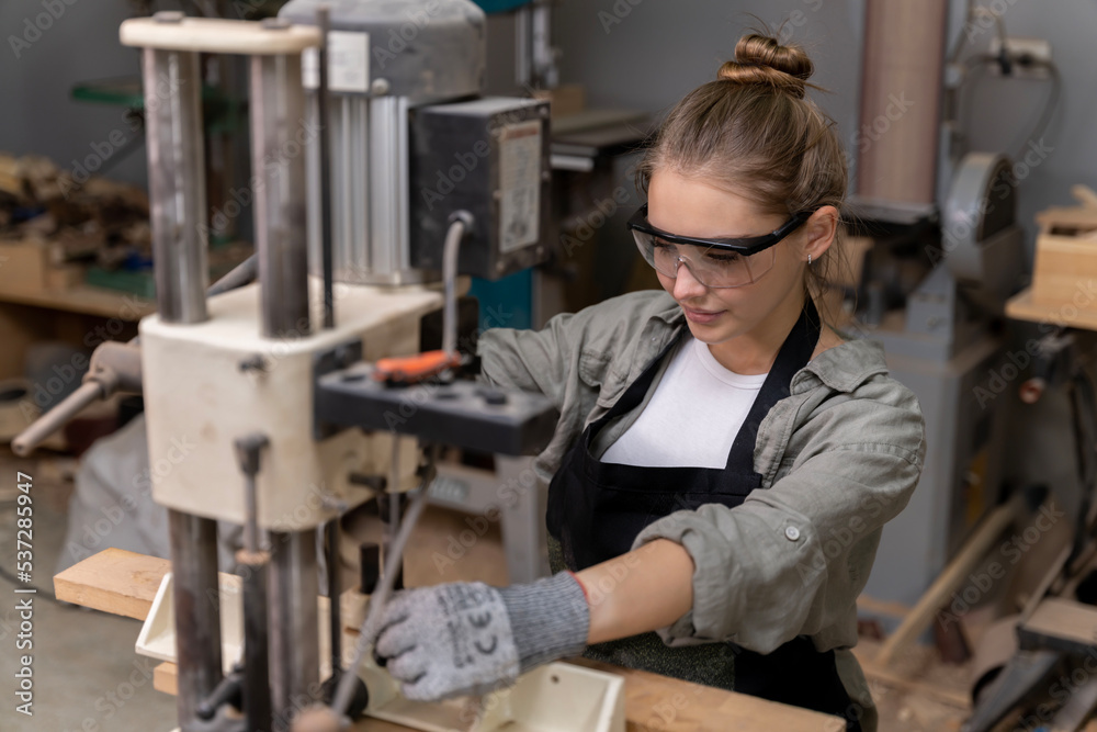 Portrait of a female carpenter using tools or machines for cutting, not drilling, wood to make furniture in a furniture factory. with modern tools Portrait of a female carpenter using tools or machines for cutting, not drilling, wood to make furniture in a furniture factory. with modern tools