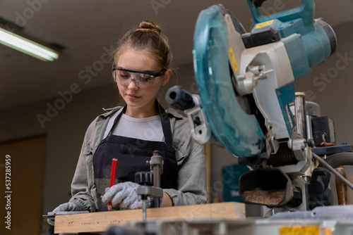 Portrait of a female carpenter using tools or machines for cutting, not drilling, wood to make furniture in a furniture factory. with modern tools