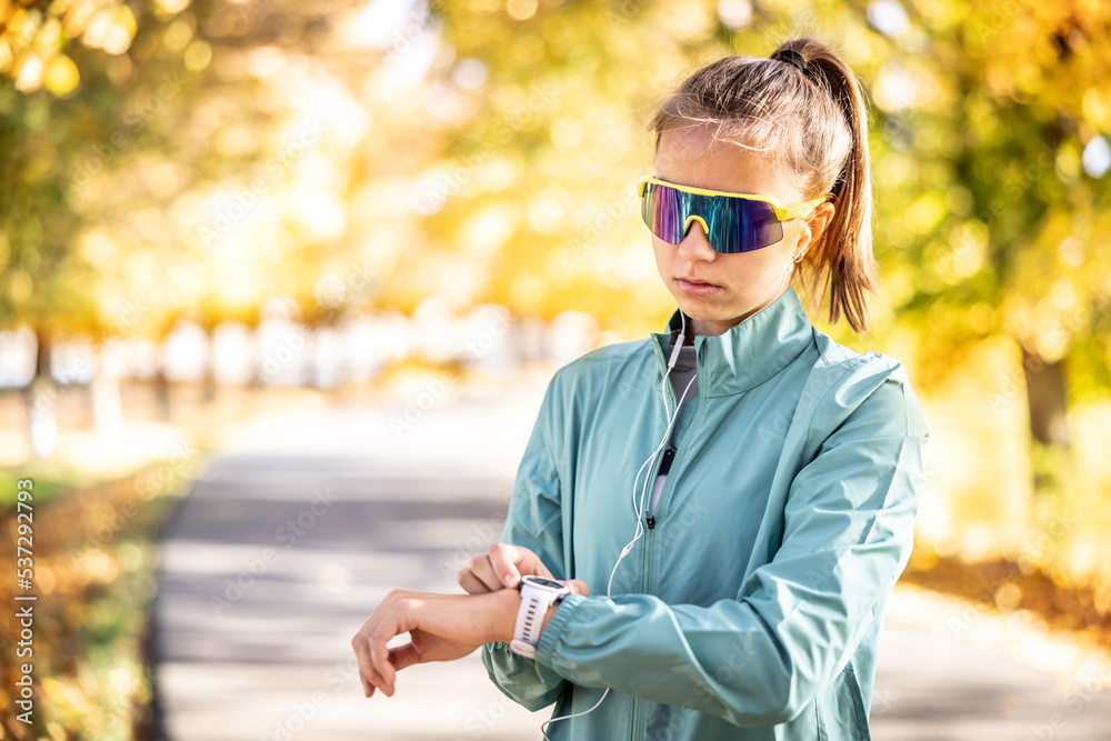 Woman sporting outdoors wears earphones and looks at the smartwatches on her wrist Woman sporting outdoors wears earphones and looks at the smartwatches on her wrist