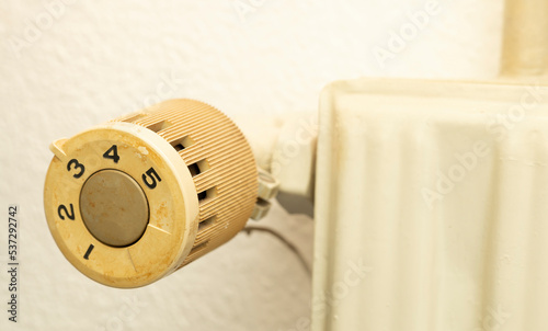 Closeup of old radiator heating in house with white wall background.  Knob with number to be adjust and control temperature in room in winter, energy bill expenses household