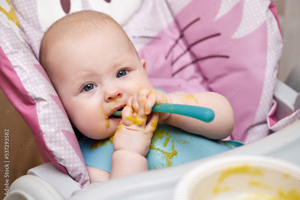 baby girl eating with spoon in kitchen baby girl eating with spoon in kitchen