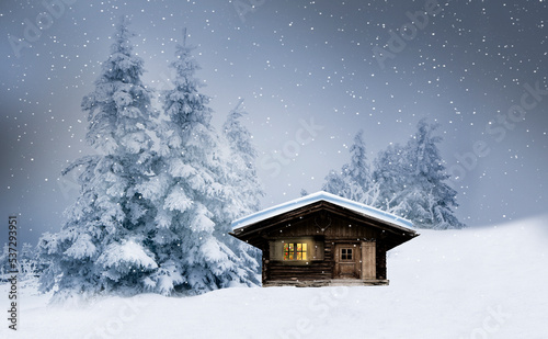 Glänzender Weihnachtsbaum bein einer Blockhütte im Schnee