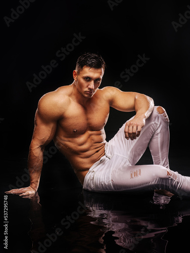 Obraz na płótnie Shirtless muscular man in white jeans sitting  in water