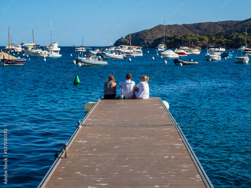 Tres jóvenes turistas sentados en el borde de un muelle de madera de Cadaqués