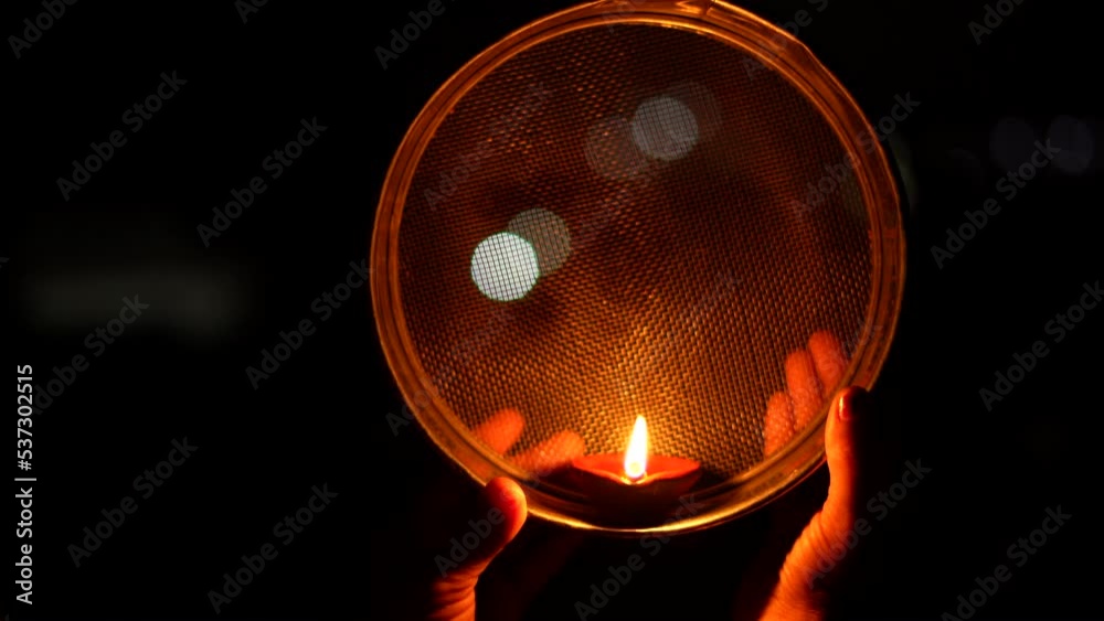 Woman hand holding Karwa Chauth strainer for the Karwa Chauth celebration on the night. Karwa Chauth strainer and Diya oil lamps for the Karwa Chauth celebration on the night