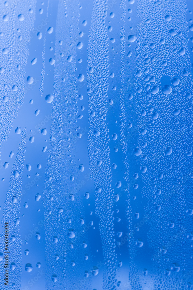 Close-up of raindrops on a window pane. Gloomy wet weather. Drops of water on glass in front of dark blue rain clouds. Rain. Abstract background texture. High quality photo