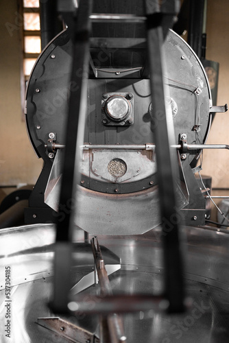 White coffee beans are resting inside of a big coffee roaster machine