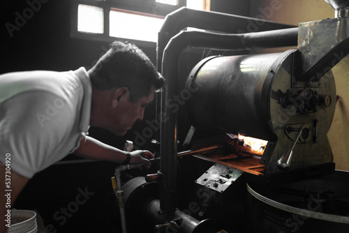 An Hispanic man is checking the burner of a coffee roaster machine