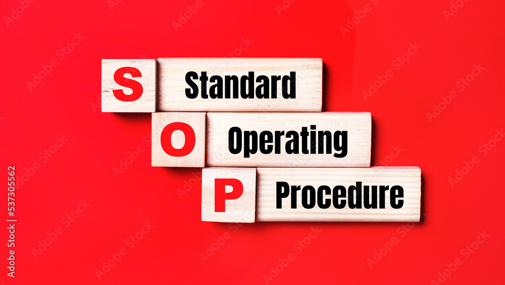 On a bright red background, wooden cubes and blocks with the text SOP Standard Operating Procedure. Manufacturing of wooden toys. On a bright red background, wooden cubes and blocks with the text SOP Standard Operating Procedure. Manufacturing of wooden toys.