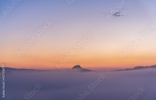 Mountain peak in clouds twilight sunrise sky. View of mountain peak in fog. Beautiful landscape of foggy hills. © torjrtrx