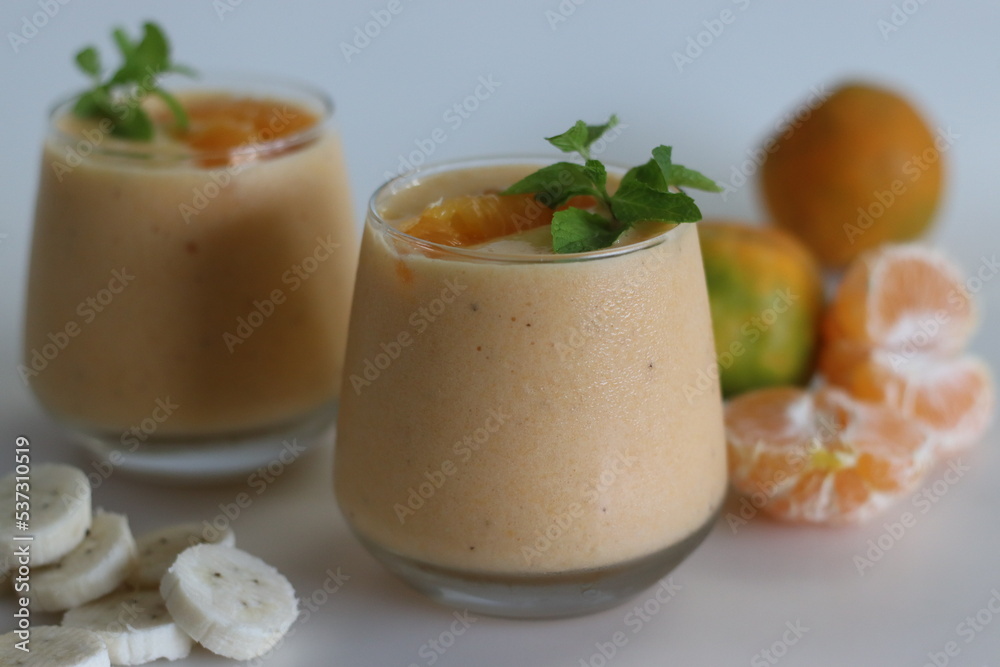 Orange banana smoothie. Summer drink smoothie made of frozen bananas and fresh orange in almond milk, garnished with mint leaves Orange banana smoothie. Summer drink smoothie made of frozen bananas and fresh orange in almond milk, garnished with mint leaves