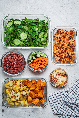 Vegan meal prep containers with  marinated tofu  beans  baked vegetables  green salad and vegetable sticks.
